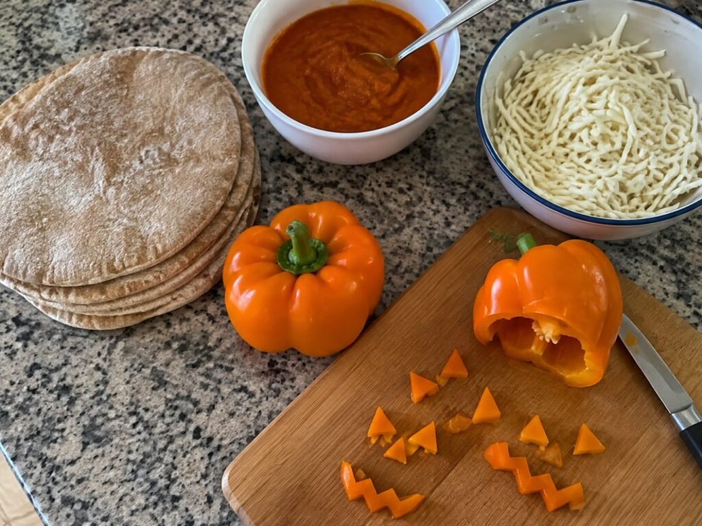 Ingredientes para mini pizzas de Halloween: pan pita integral, pimiento naranja cortado en caritas, salsa de jitomate y calabaza y mozzarella