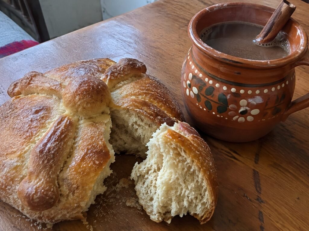 Pan de muerto integral partido mostrando su miga suave y esponjosa junto a un jarrito de café de olla humeante con canela