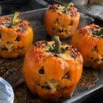 Pimientos naranjas tallados como calabaza, recién salidos del horno, rellenos de pavo y arroz con queso derretido para una cena de Halloween saludable