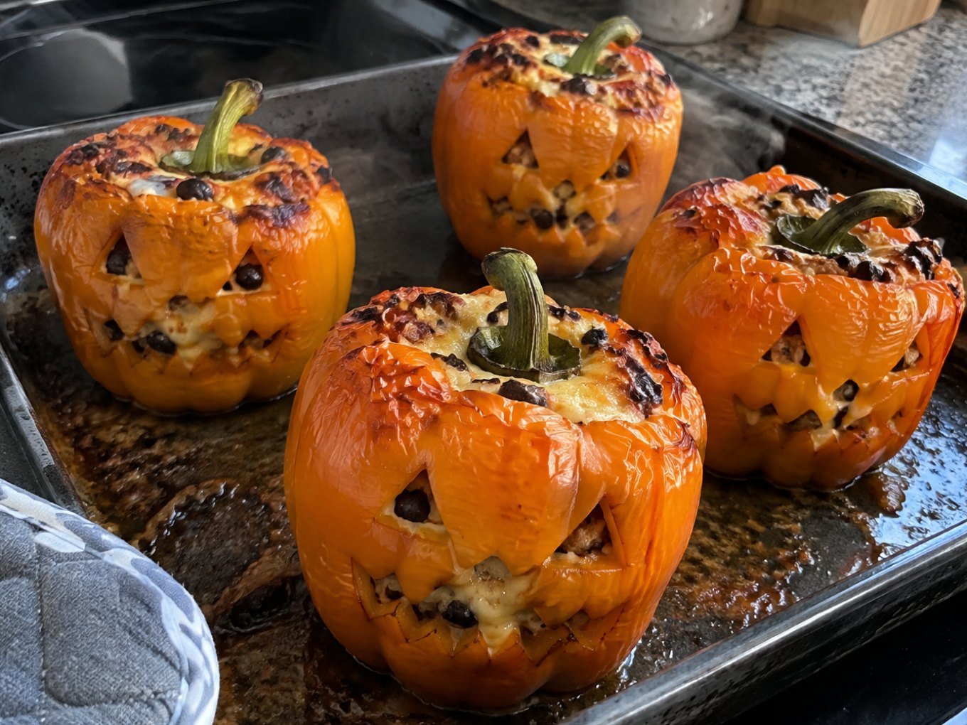 Pimientos naranjas tallados como calabaza, recién salidos del horno, rellenos de pavo y arroz con queso derretido para una cena de Halloween saludable