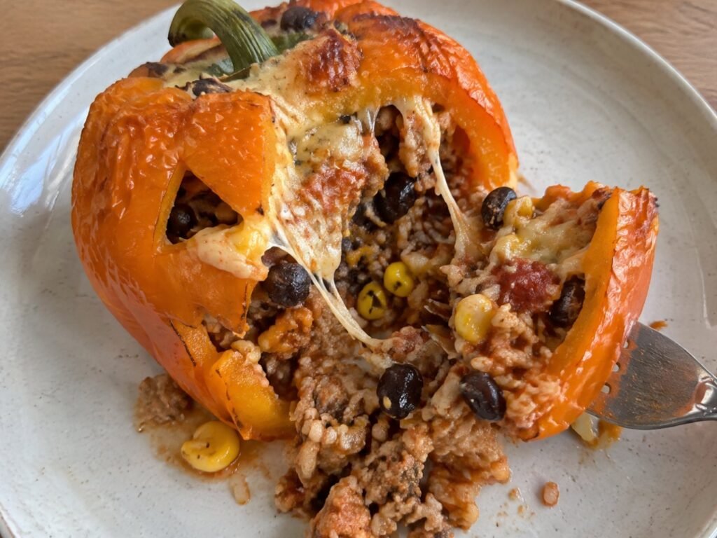 Pimiento relleno partido con tenedor mostrando el relleno jugoso de pavo, arroz, frijoles negros y elote con queso que se estira, cena fácil