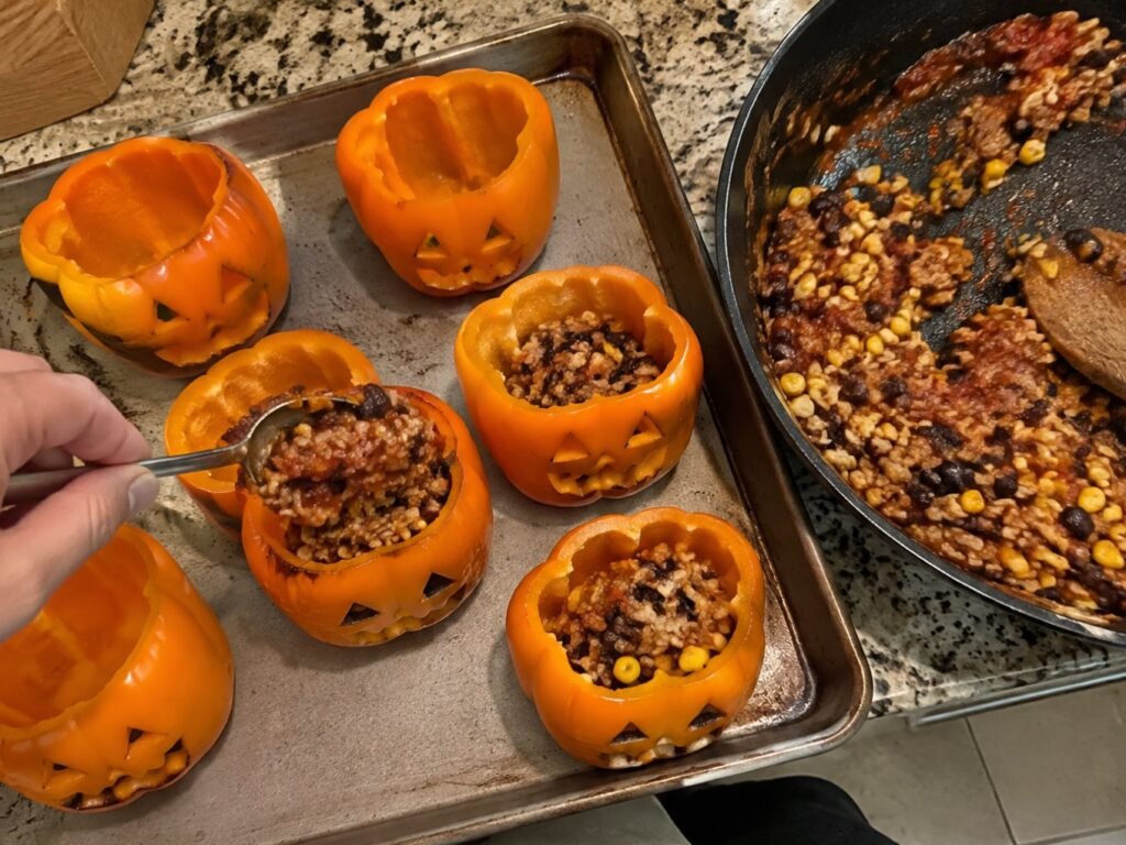 Mano rellenando pimientos naranjas tallados como calabaza con relleno de pavo molido y arroz desde el sartén, preparación de cena de Halloween