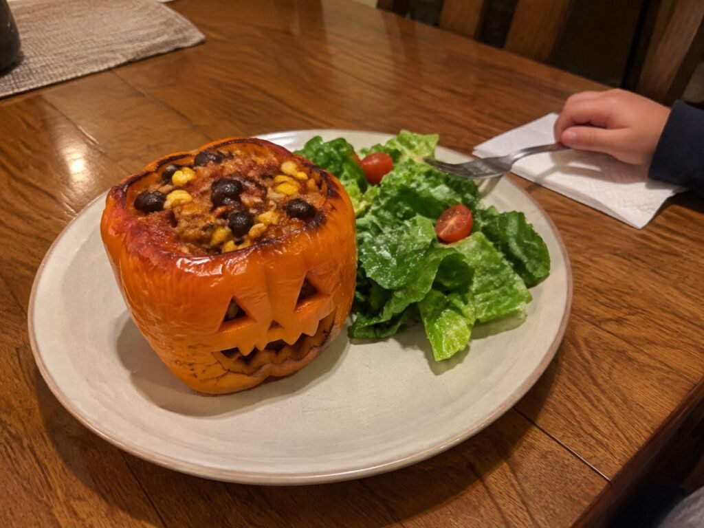 Pimiento relleno Jack-o'-Lantern servido en plato con ensalada verde en la mesa familiar, cena de Halloween saludable y alta en proteína para niños