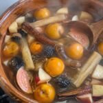 Olla de barro con ponche navideño de frutas sin azúcar humeante, con tejocotes, guayaba, caña y canela sobre la estufa de casa