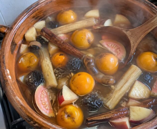 Olla de barro con ponche navideño de frutas sin azúcar humeante, con tejocotes, guayaba, caña y canela sobre la estufa de casa