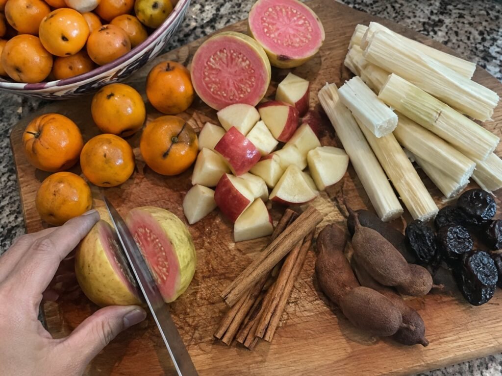Ingredientes del ponche navideño en tabla de madera: guayabas, tejocotes, manzana, caña pelada, canela y tamarindo en la cocina