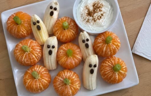 Plato casero con mandarinas peladas como calabacitas con tallo de apio, plátanos fantasma con ojos de chocolate y dip de yogur con canela