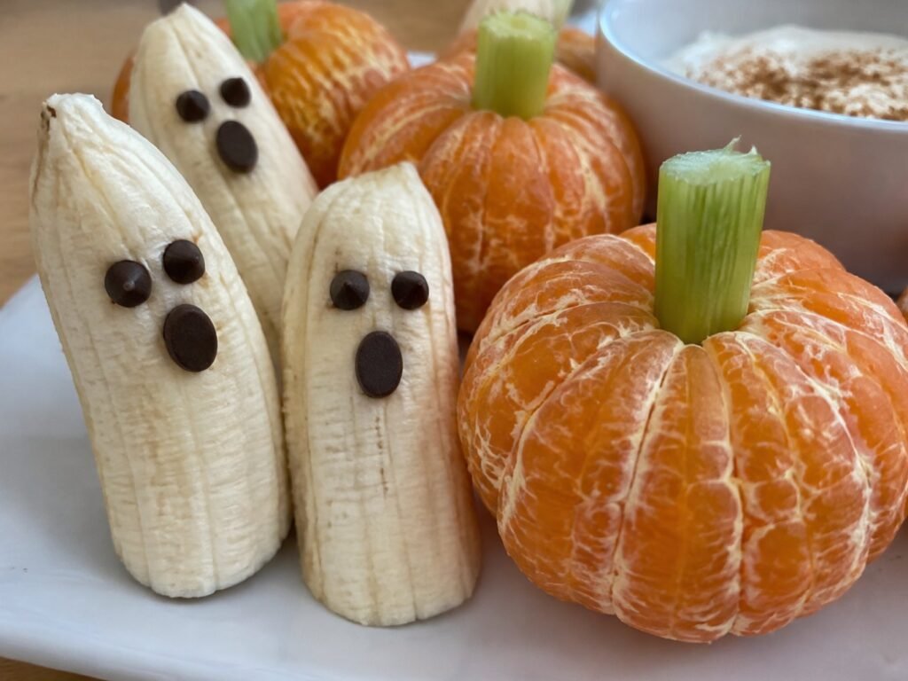 Close-up de plátanos fantasma con caritas de chispas de chocolate amargo junto a una mandarina calabaza, snack de Halloween sin azúcar
