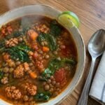 Sopa de lentejas con chorizo de pavo y espinaca servida en plato hondo humeante sobre mesa de madera, receta fácil y saludable