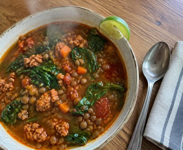 Sopa de lentejas con chorizo de pavo y espinaca servida en plato hondo humeante sobre mesa de madera, receta fácil y saludable