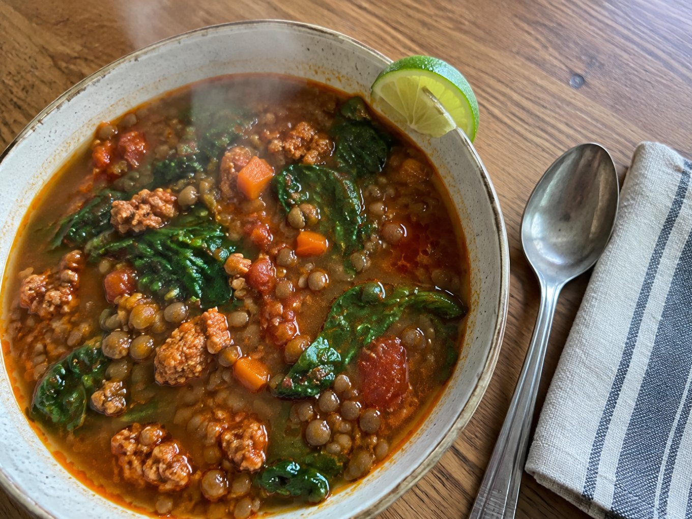 Sopa de lentejas con chorizo de pavo y espinaca servida en plato hondo humeante sobre mesa de madera, receta fácil y saludable