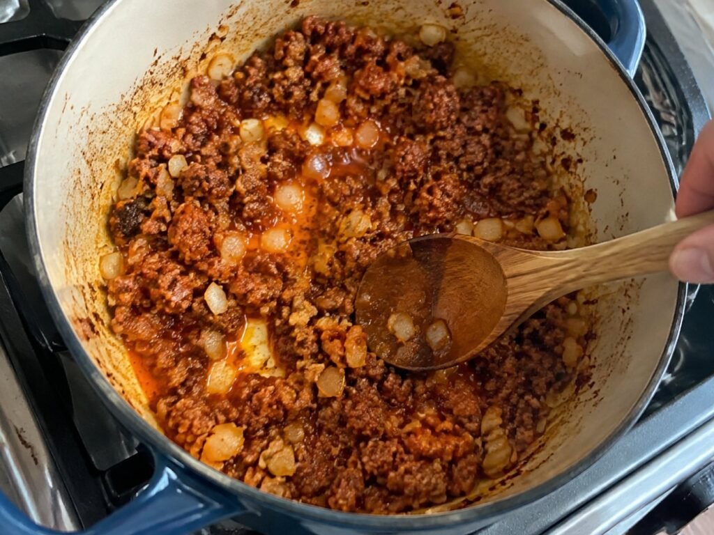 Chorizo de pavo dorándose con cebolla y ajo en olla sobre la estufa, primer paso de la sopa de lentejas casera fácil