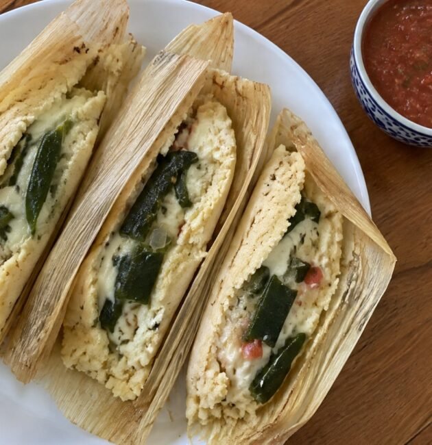 Tamales de rajas con queso sin manteca abiertos en plato blanco, masa esponjosa con chile poblano y queso derretido, receta casera
