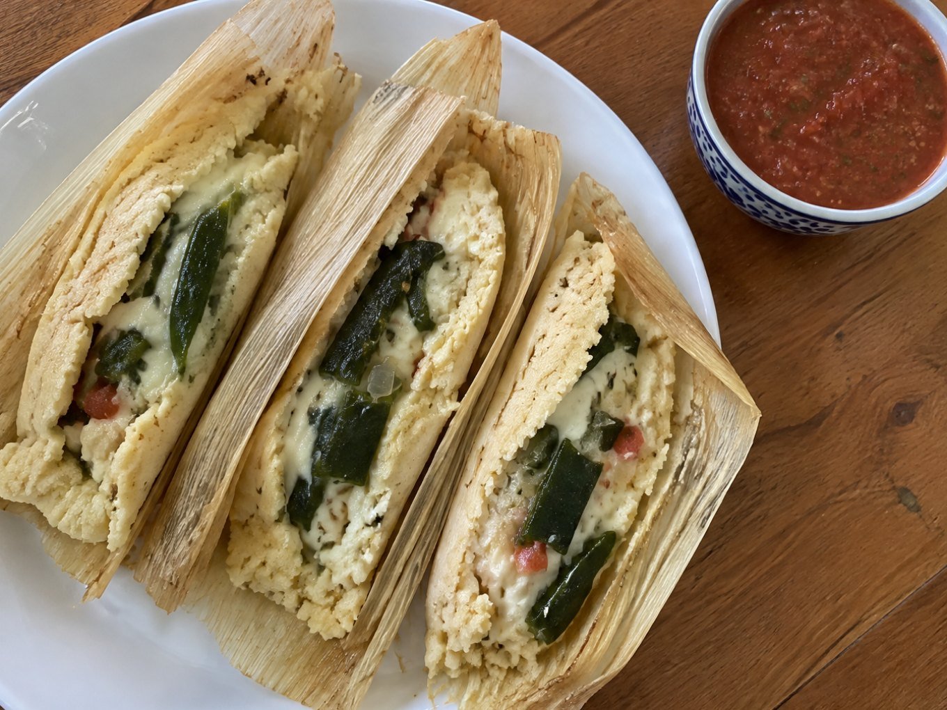 Tamales de rajas con queso sin manteca abiertos en plato blanco, masa esponjosa con chile poblano y queso derretido, receta casera