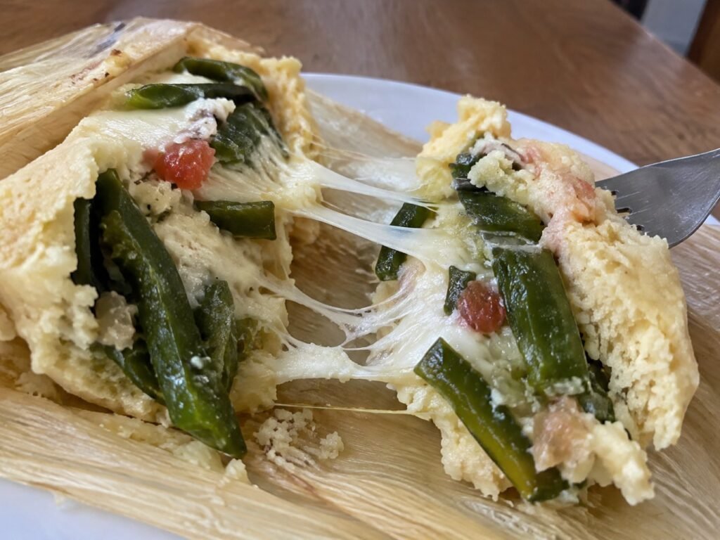 Tamal de rajas con queso partido con tenedor, queso Oaxaca derretido estirándose y rajas de poblano, tamales saludables caseros