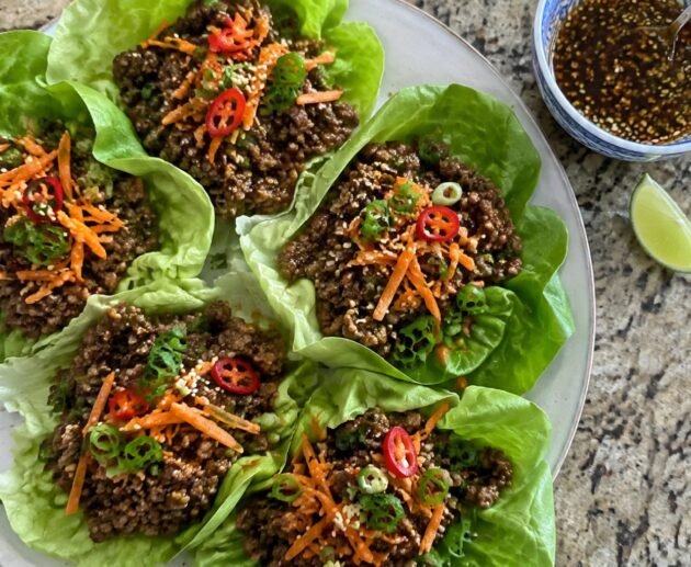 Wraps de lechuga rellenos de carne molida en salsa de soya y jengibre con zanahoria, cebolla cambray y ajonjolí en un plato