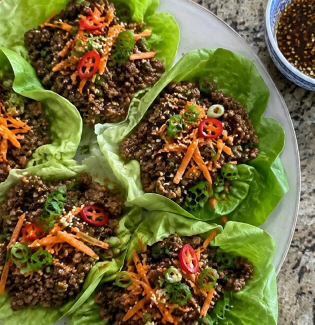 Wraps de lechuga rellenos de carne molida en salsa de soya y jengibre con zanahoria, cebolla cambray y ajonjolí en un plato