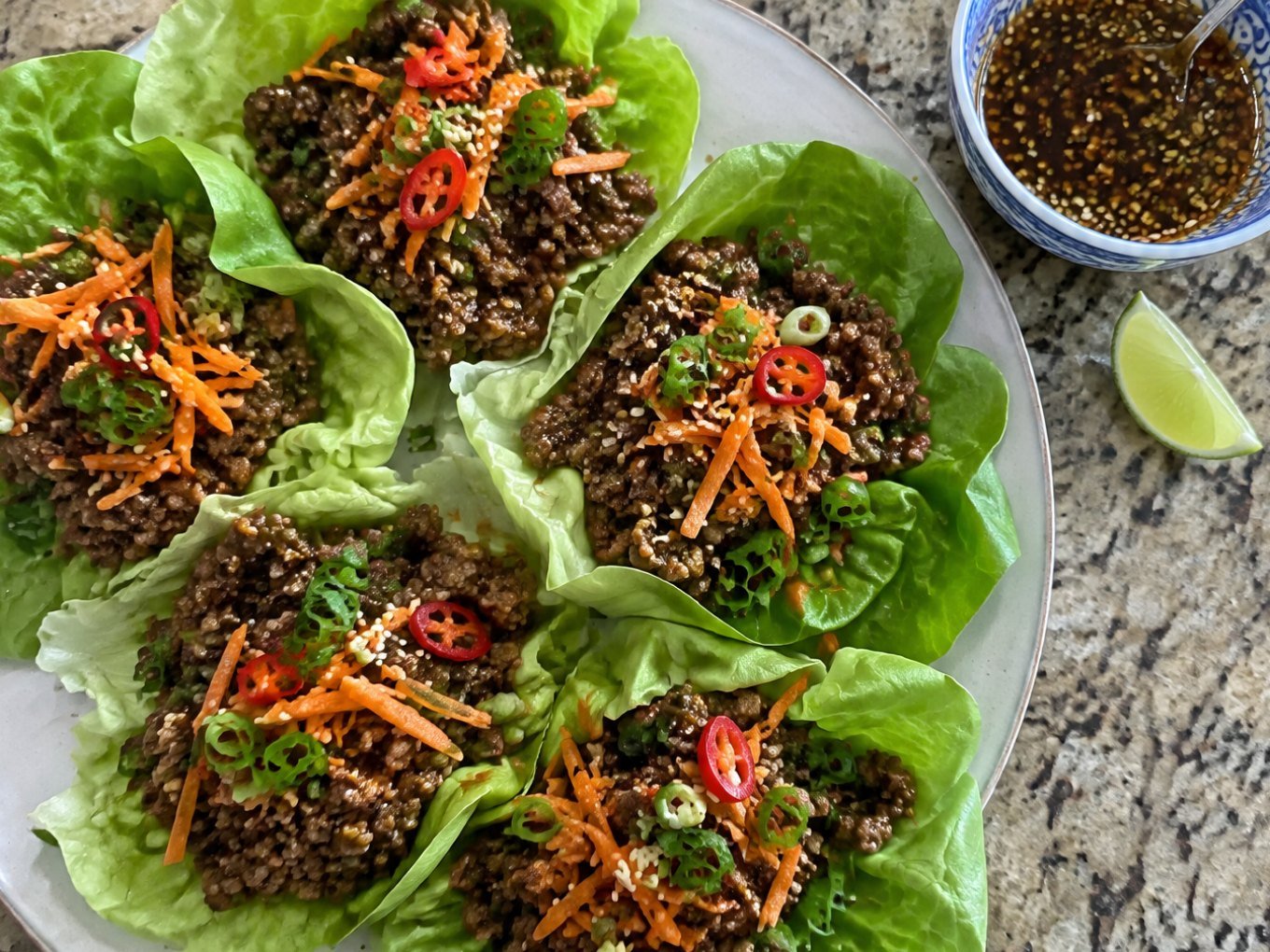 Wraps de lechuga rellenos de carne molida en salsa de soya y jengibre con zanahoria, cebolla cambray y ajonjolí en un plato